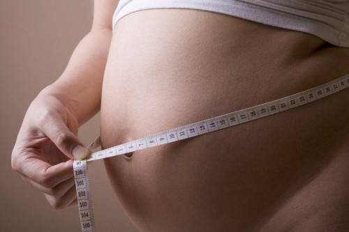 Pregnant woman measuring her belly while standing