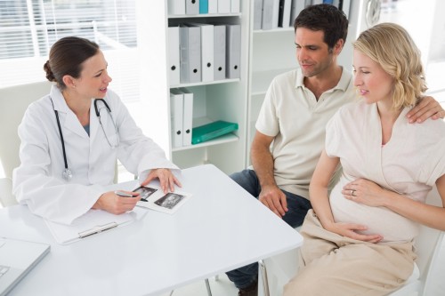 High angle view of female gynaecologist explaining reports to expectant couple in clinic