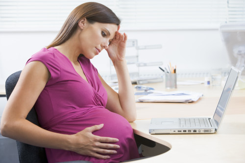 Pregnant woman at work with laptop looking stressed