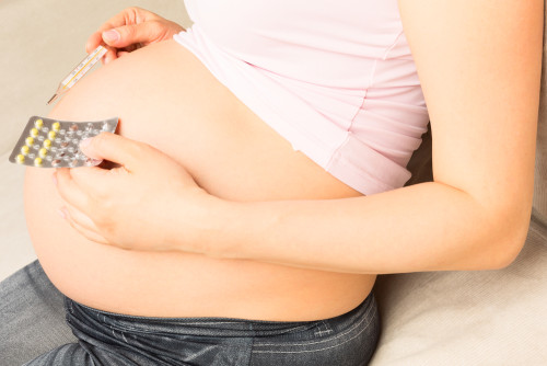 Belly of Pregnant Woman Sitting on a Couch and Holding Thermometer and Pills in Blister Package