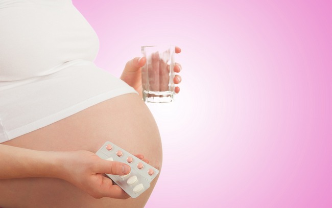 belly of pregnant woman and vitamin pills and glass of water in the hand