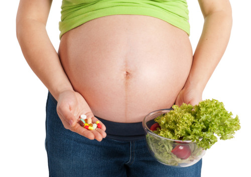 Pregnant woman holding salad in one hand and pills on another