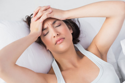 High angle view of a sleepy young woman suffering from headache with eyes closed in bed at home