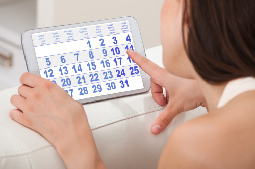Cropped image of young woman using calendar on digital tablet at home