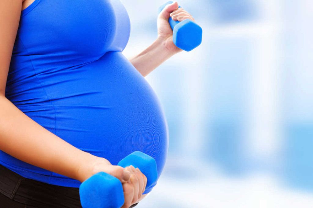 Pregnant female do exercise in sports hall, side view, body part, lifting dumbbells, active and sportive pregnancy, healthy motherhood concept