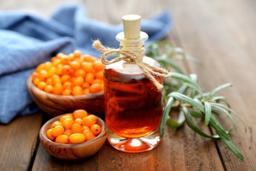 Sea-buckthorn oil and berries in bowl on a wooden background