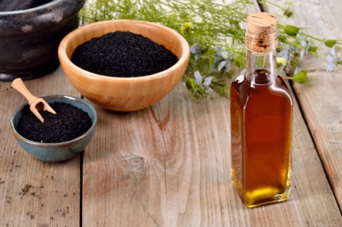 Nigella sativa oil in a bottle and nigella seeds and flowers on wooden background. Black cumin healing herb. Cold pressed, non refined oil. Traditional medicine.