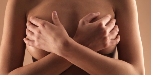 Naked young woman holding hands over breasts, mid section, front view