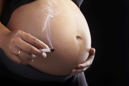 Pregnant lady's stomach and her hand holding a burning cigarette over black background