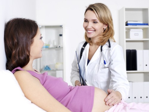 Happy doctor caring about young pregnant woman in hospital
