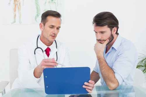 Male doctor discussing reports with patient at desk in medical office