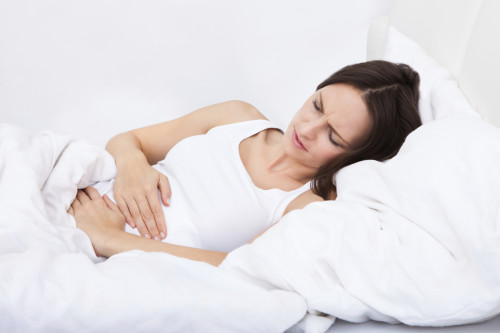 Woman with stomach ache lying on bed