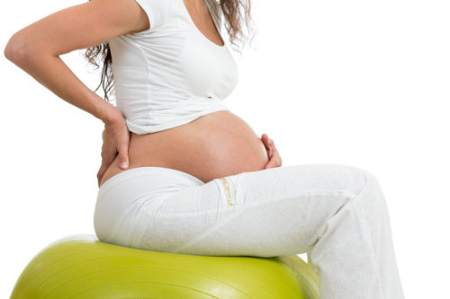 pregnant woman sitting on fit ball with hand on her back, isolated