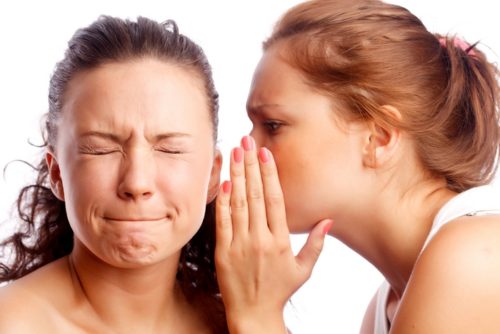 Young woman whispering something to her frind. Isolated over white.