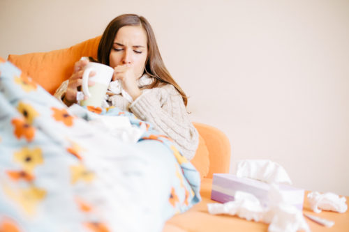 Sick young woman is coughing on the couch