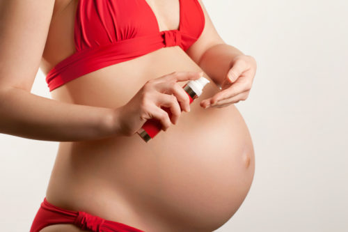 Skin care in pregnancy concept: young woman with body cream, closeup shot