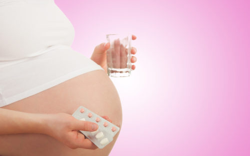 belly of pregnant woman and vitamin pills and glass of water in the hand